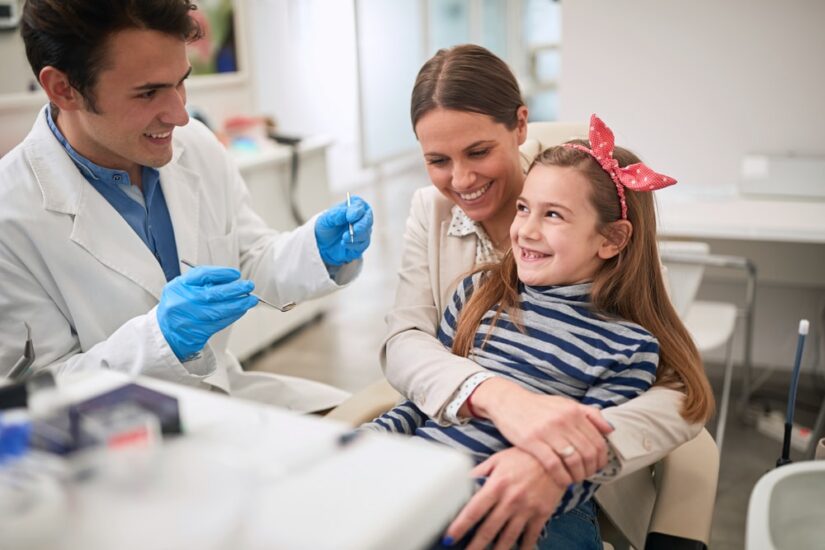 Family in dentist’s office. Dentist examining his smiling girl patient in dentist’s clinic