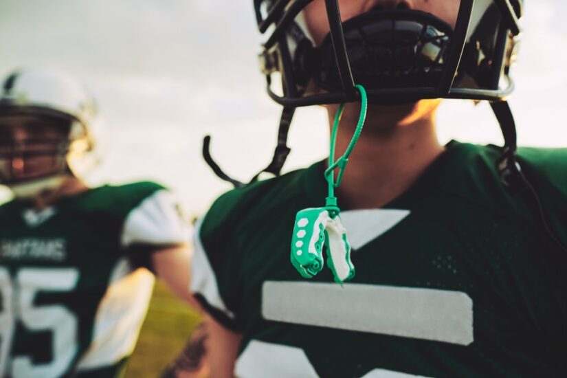 Closeup of a young American football player with his mouthguard hanging from his helmet during an afternoon practice